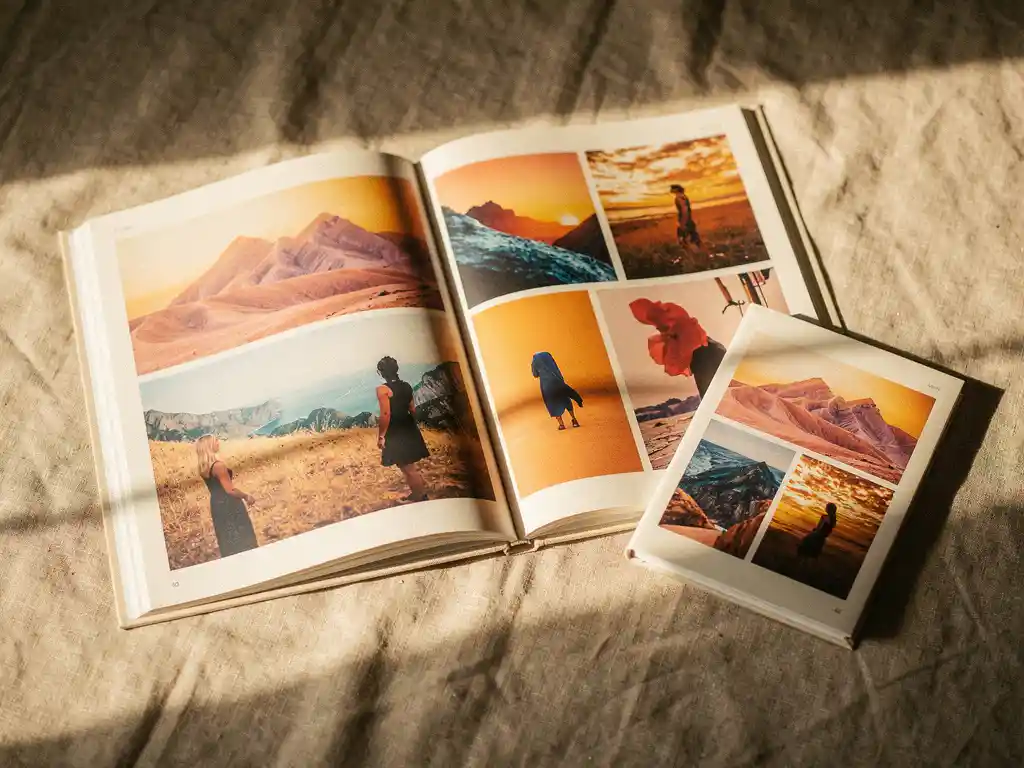 Three open photo books of varying sizes on linen, the largest showing vibrant travel spreads, bathed in warm afternoon light.